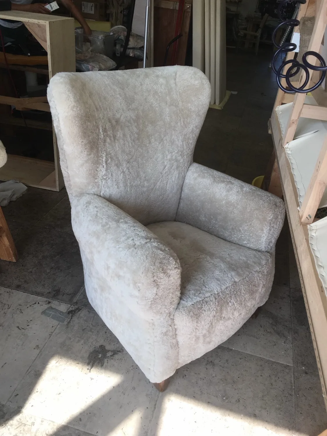 A wingback chair upholstered in soft grey shearling, finished in the shop